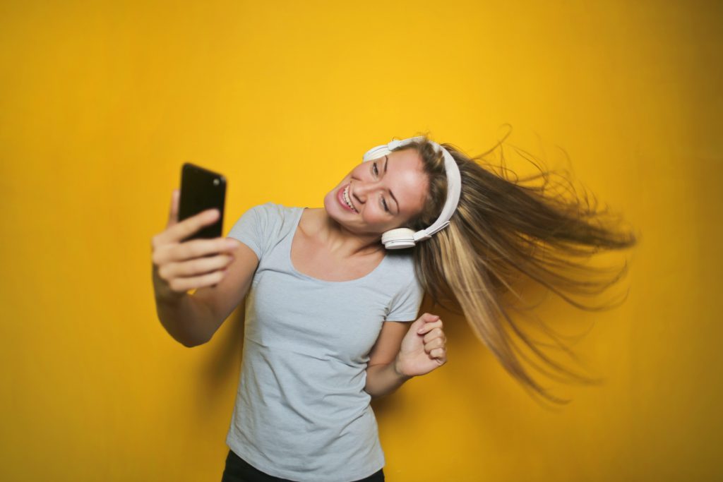 Image of a girl with headphones on, looking at her phone, on a yellow background