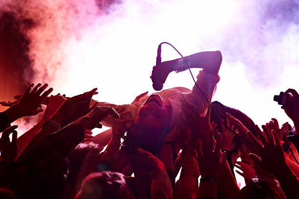Person crowd surfing with microphone in hand. Red smoke in the background.