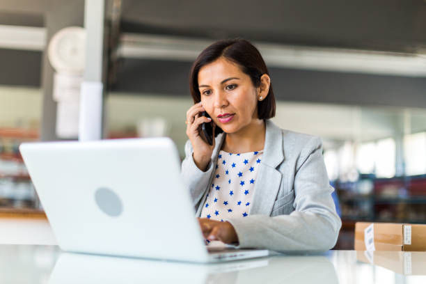 Lady on the phone with a blurred background, looking at her laptop.