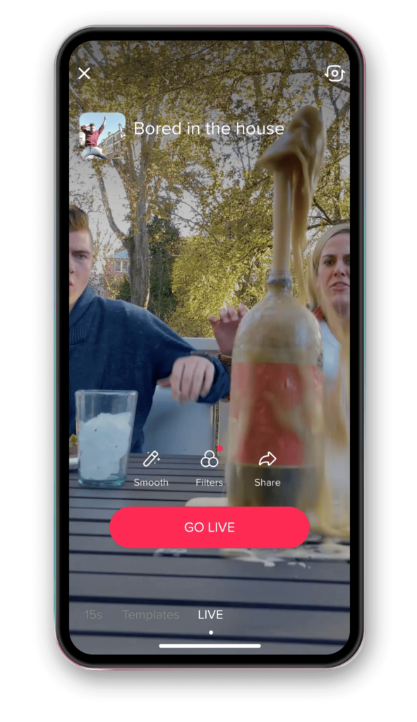 Smartphone displaying a TikTok live of a man and woman doing a challenge where a bottle of fizzy drink explodes.