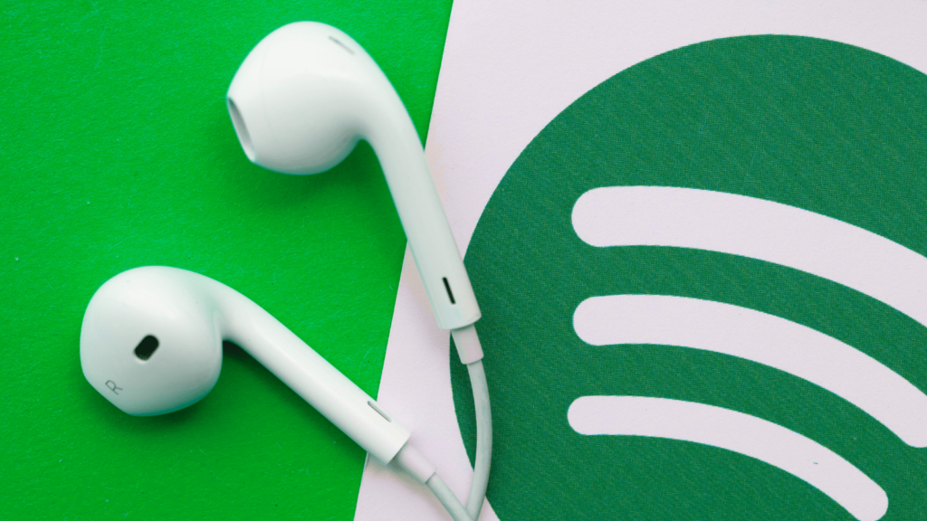 Green background with Spotify logo on a card, next to a pair of earphones.