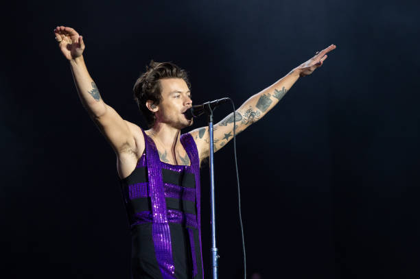 Harry Styles with his arms in the air singing into a microphone