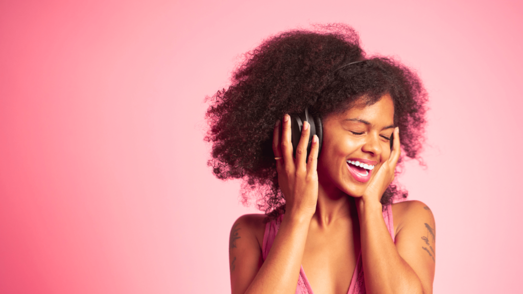 Girl happy listening to music through her headphones. Against a pink lit background.