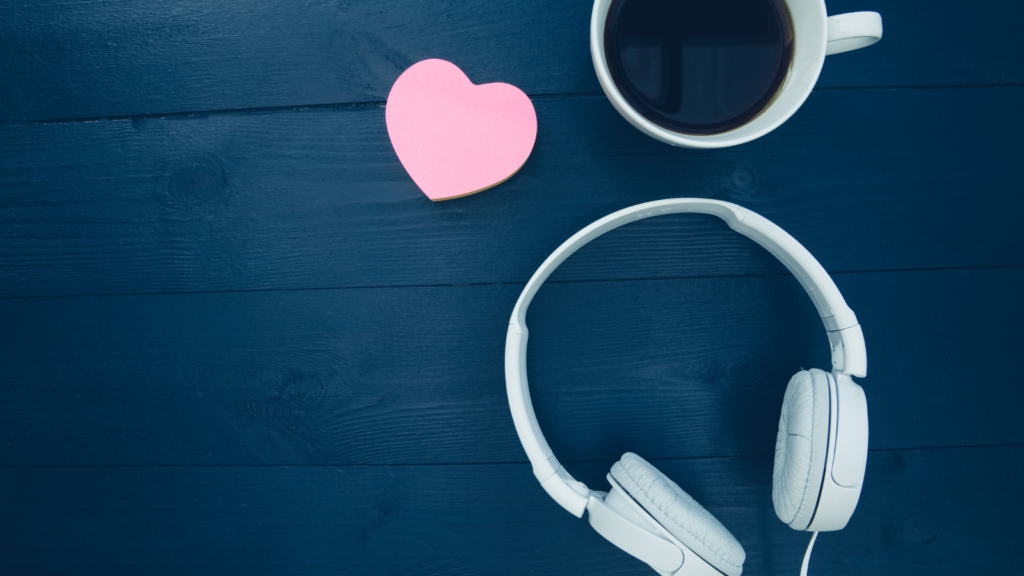 Blue wooden background. In the foreground are headphones, a coffee and a heart.