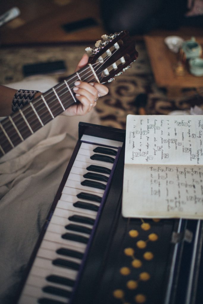 Image of a keyboard, with someone holding a guitar and written music lay in front of them.