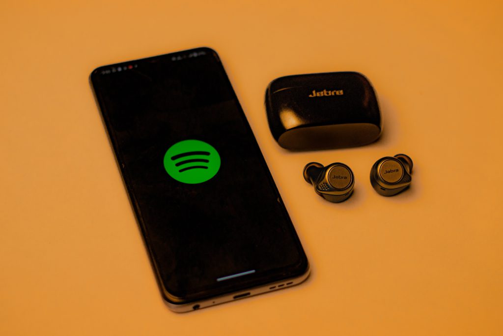 Spotify loaded on a smartphone with earphones next to it. Against an orange background.