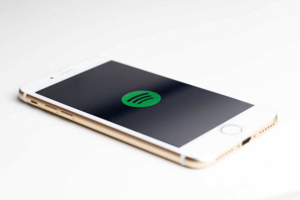 Spotify translates podcasts into multiple languages with AI voice cloning: iPhone laid down with Spotify logo loaded.