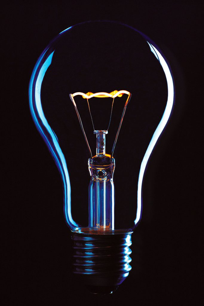 A guide to finding inspiration for your next blog article. Black background. In the foreground is a lightbulb lit up.