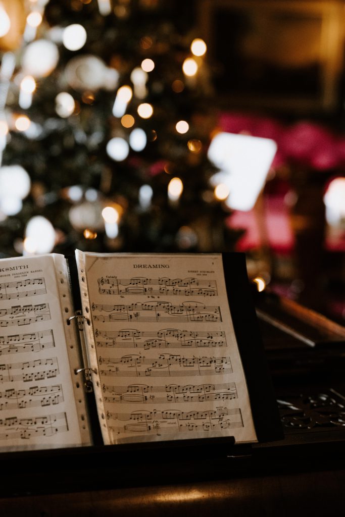 Festive ways for music artists to promote their tracks this Christmas. Photo of sheet music on a piano with a Christmas tree behind.