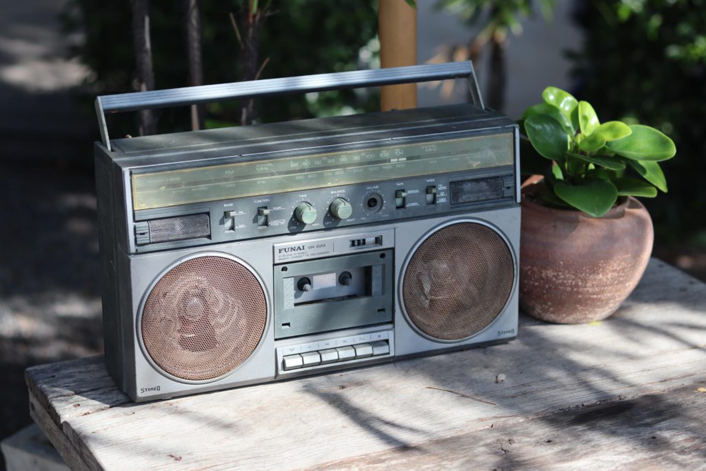 A beginner's guide to becoming a radio broadcast assistant. Photo of a radio on a plank of wood outside by a plant pot.