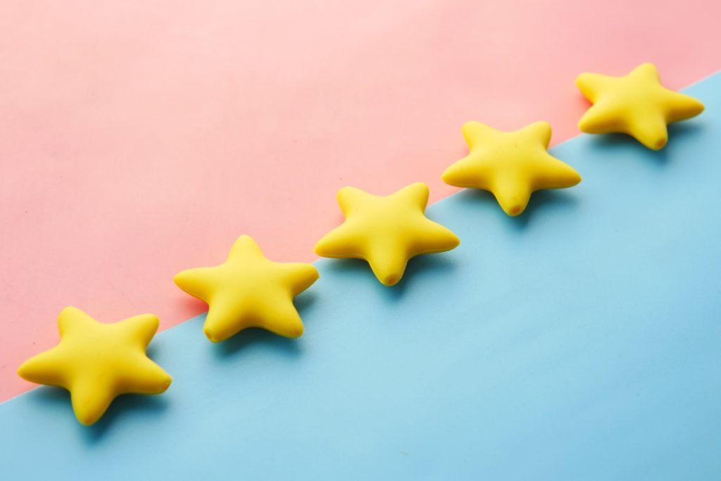 The power of feedback for small businesses. Photo of half a pink and half a blue background, split diagonally. Across the split are 5 3D yellow stars.