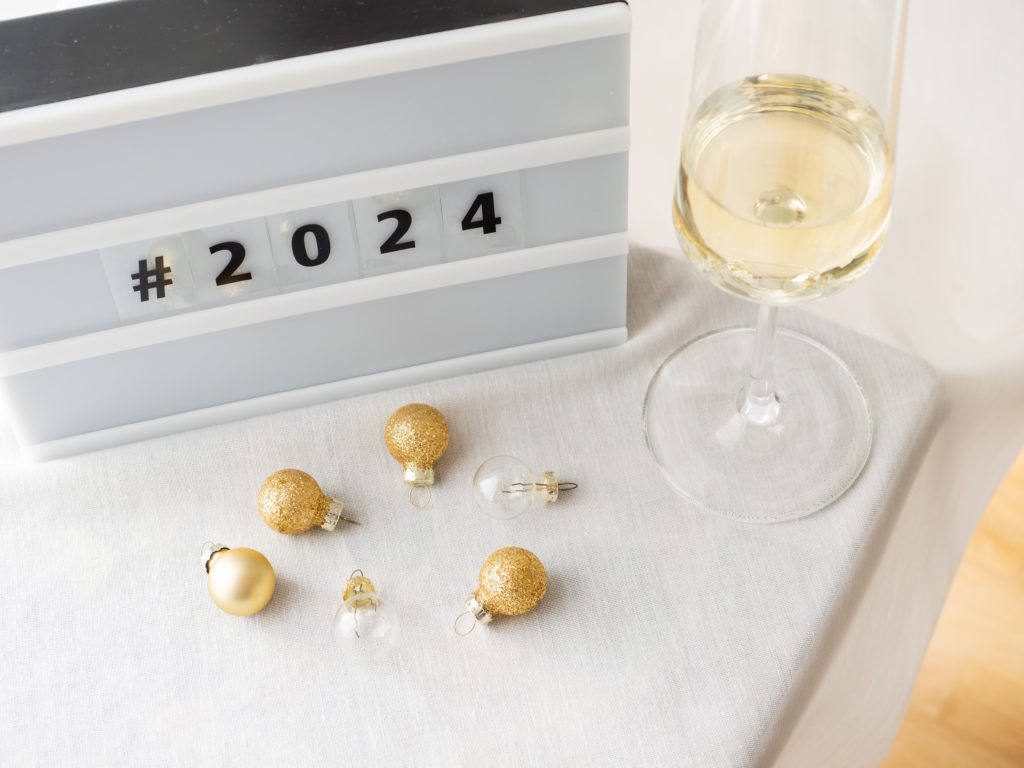 3 New Year's resolutions for small businesses. Photo of a board saying #2024 and a glass of wine with some tiny baubles.