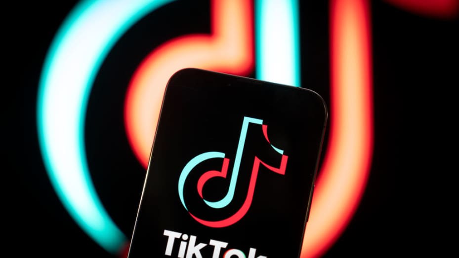 TikTok is set to become the highest-grossing app of 2024 due to $10 billion in consumer spending. Black background with neon blurred TikTok logo. In the foreground is the TikTok logo on a smartphone.