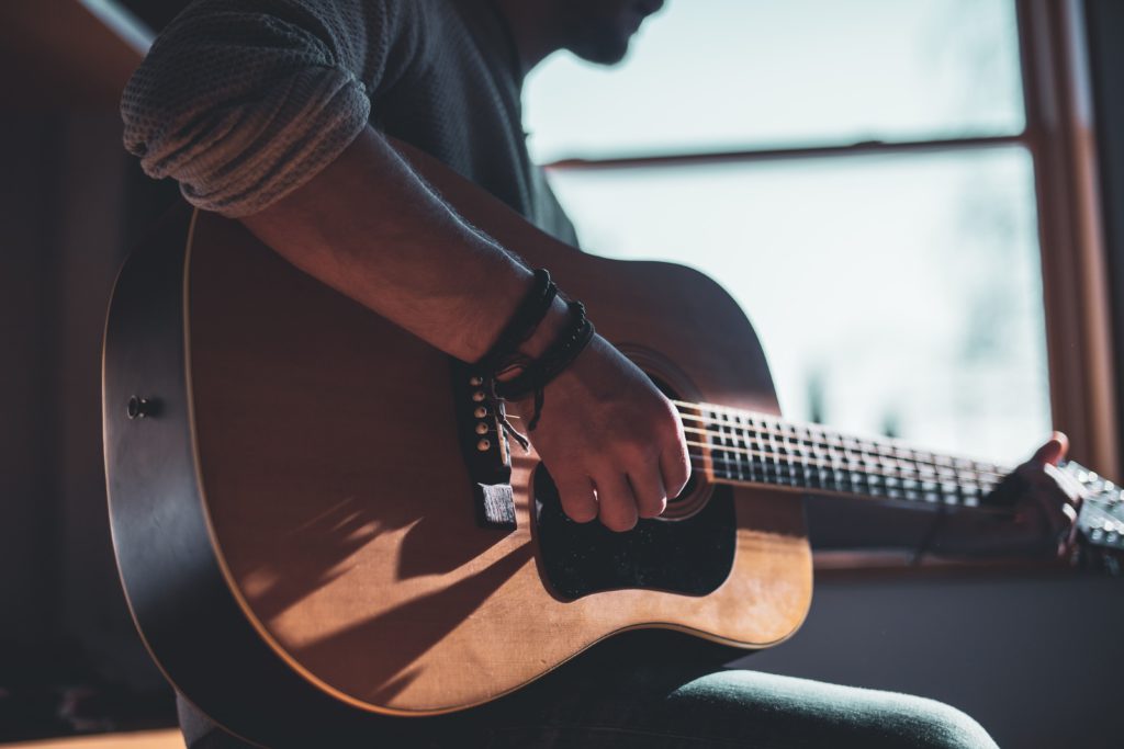 Beginner musicians - how do you pick the right guitar for you? Photo of up close of a man playing guitar.
