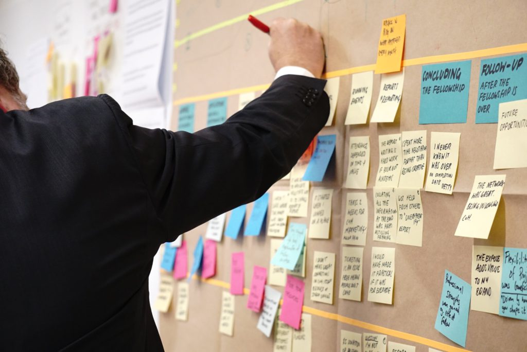 Preparation is key - a beginner's guide to content batching. Photo of a man side on writing on a post-it-note. There's a whole wall of notes with things to do on.