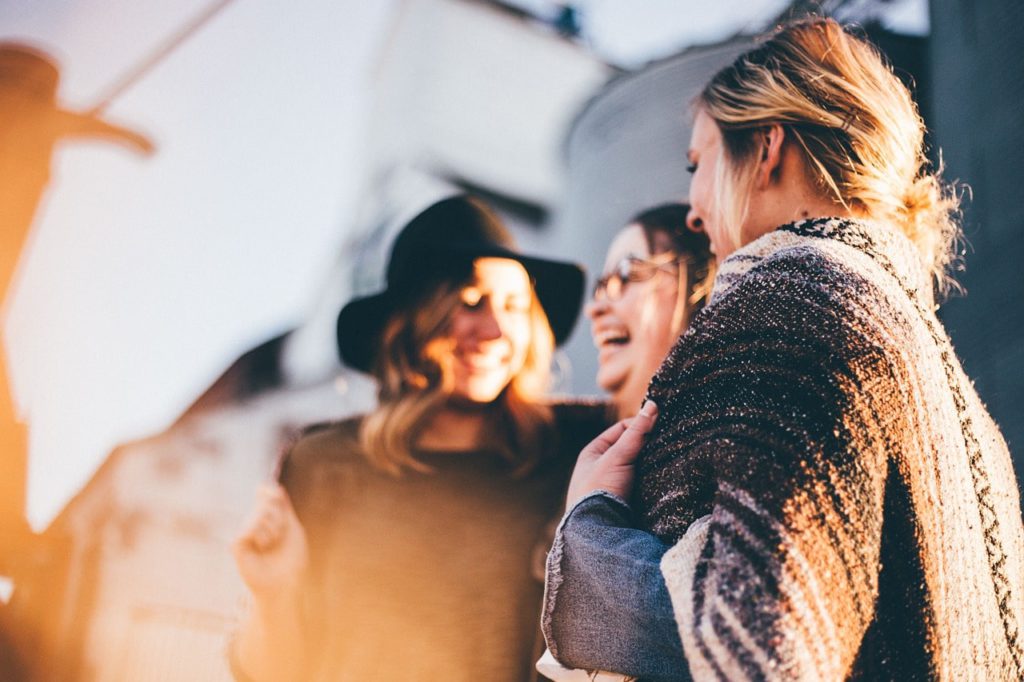 5 ways to make new friends within the music industry. Photo of three female friends laughing. They're outside but the photo is slightly out of focus.