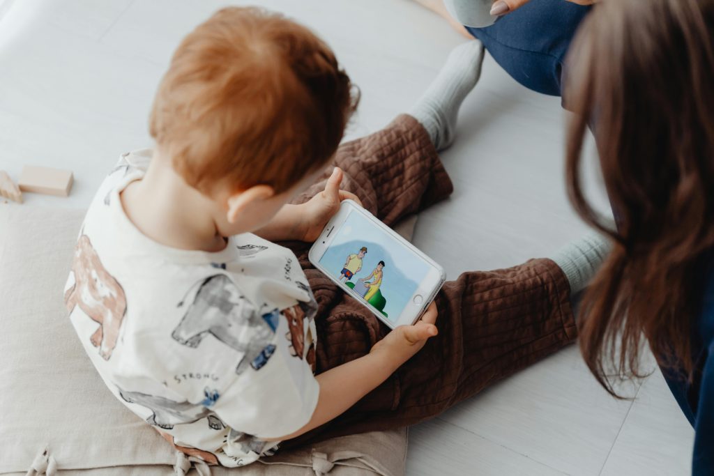 Unveiling the magic behind cartoon creation. Photo from above of a woman and her child. The child is sat on the floor watching cartoons on a smartphone.