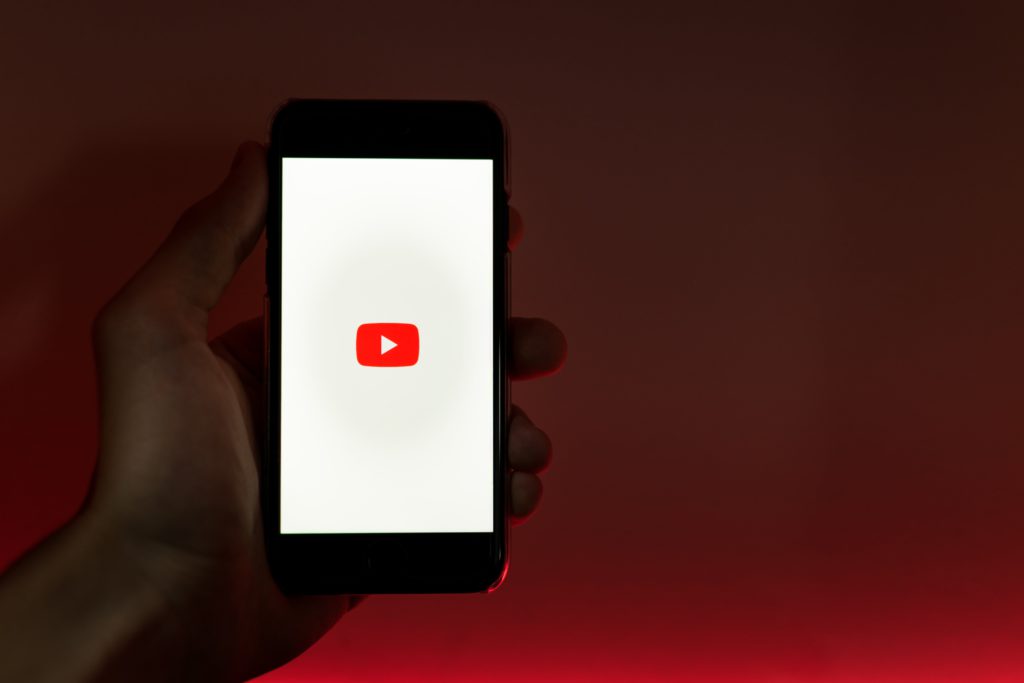 A simple guide to setting up a YouTube account. Red gradient background. Hand holding a smartphone showing YouTube's logo.