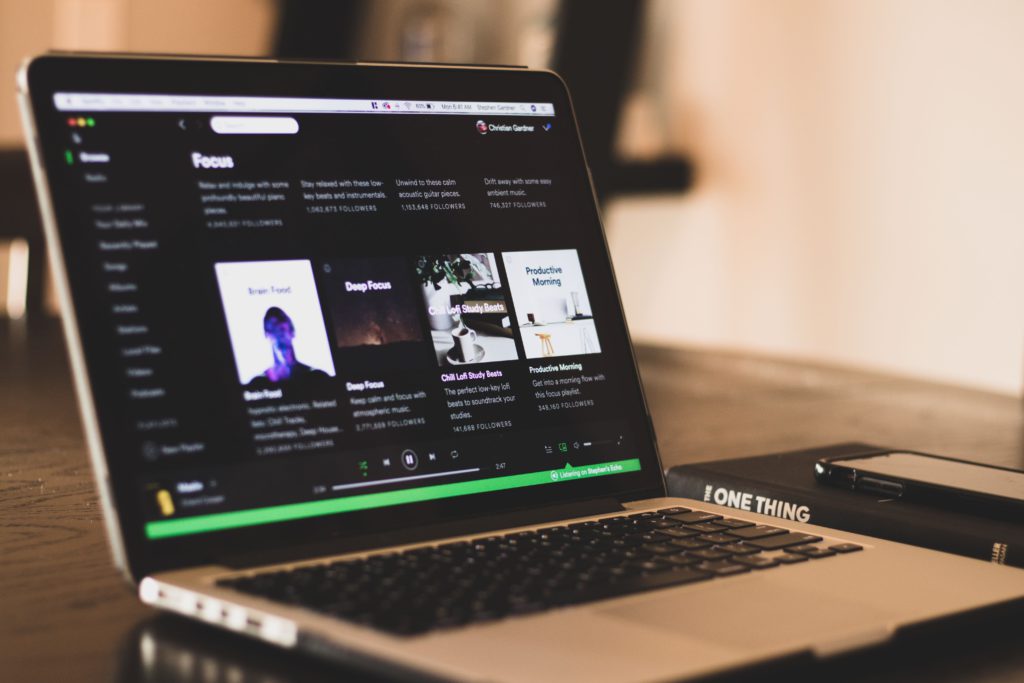 France add a tax on music streaming and Spotify aren't happy. Photo of a laptop with Spotify loaded. Next to the laptop, on the desk is a book with a smartphone on top.