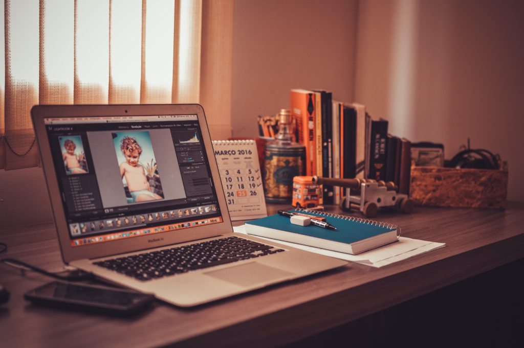 Going freelance - your beginner's guide to starting out on your own. Photo of a desk in low lighting. On the desk is a photo loaded within editing software, along with notebooks, books, a calendar and more.