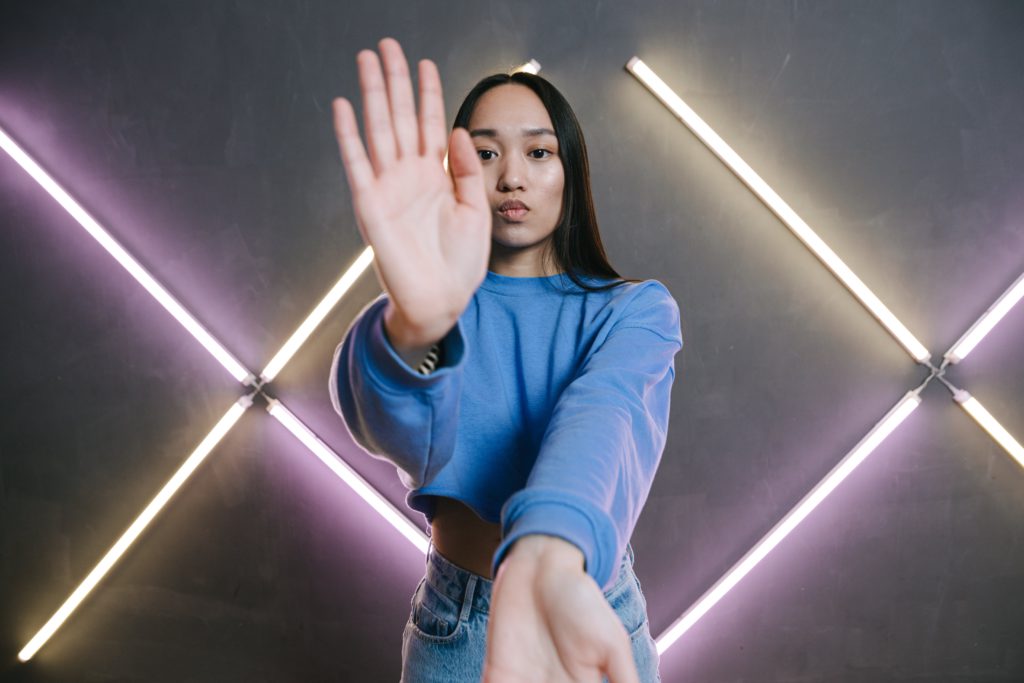 Content creators' dislikes -navigating the challenges of the online world. Photo of a girl, with her hands pointing up and down, towards the camera with lights behind her.