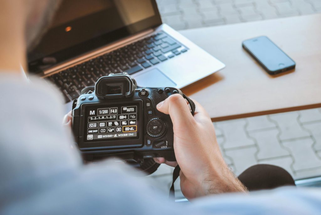 Photographer vs. photo editor - understanding the differences. Photo of a camera with the settings up, in front of a laptop.