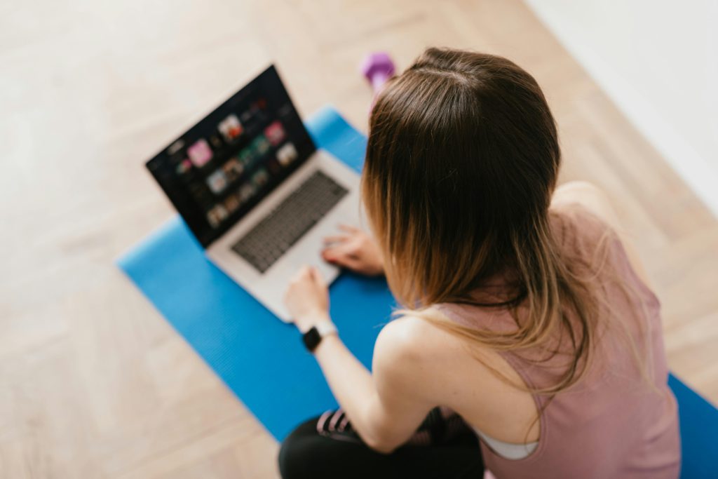 The power of promptness -responding to social media comments. Photo of a girl from above. She is sat on a yoga mat replying to her followers on her laptop.