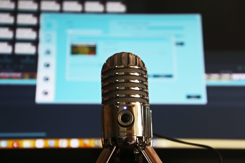 A simple beginner's guide to finding your Podcast niche. Photo of a microphone, behind it is a blurred computer screen.
