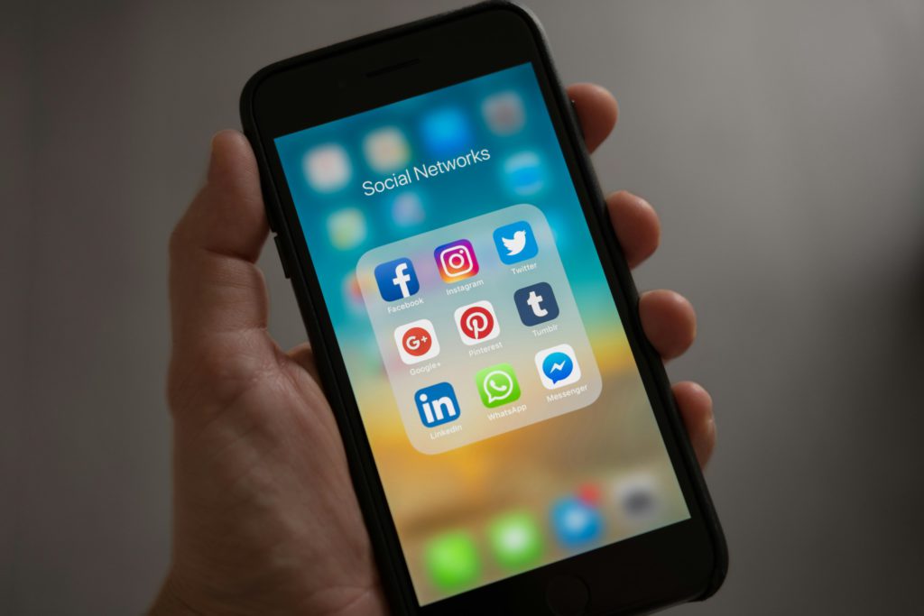 Exploring the pros and cons of boosting your social media posts. Photo of a smartphone in someone's hand. On the screen is a folder full of social media apps.