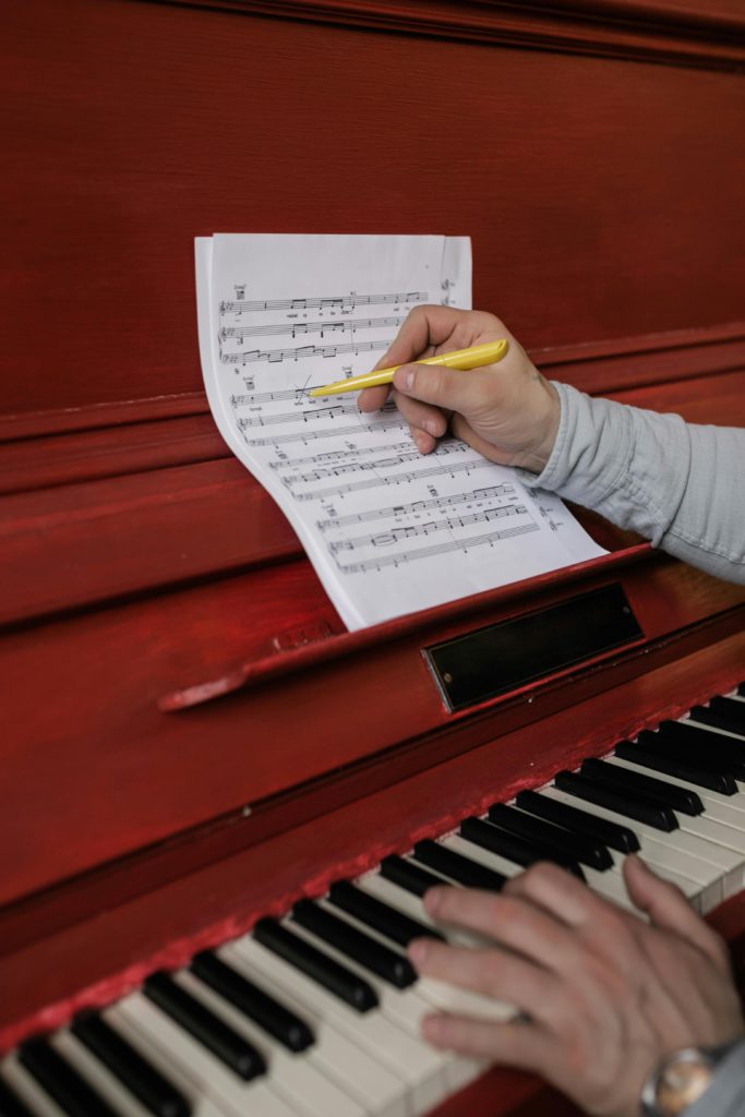 The role of a music composer -bringing soundtracks to life. Photo of someone's hand writing music onto a sheet on a piano.