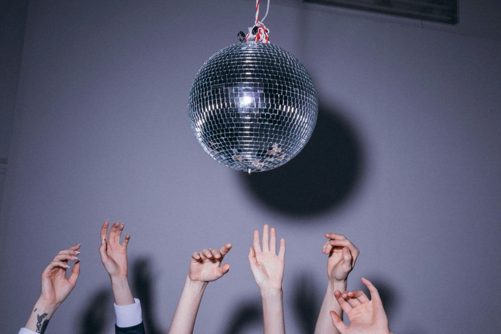 What exactly is pop music? Photo of a disco ball against a grey background. Multiple hands reaching up towards it. 