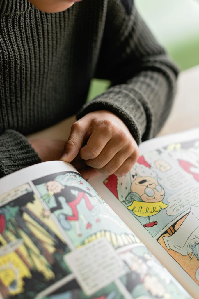 Graphic novel illustrators - what does their job role consist of? Photo of a comic book, someone's hands and torso are by the book.