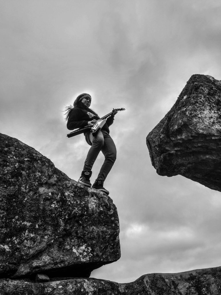 Monetising your music - strategies for generating revenue as an independent artist. Black and white photo of a musician playing the electric guitar on a rock.