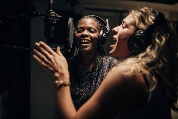 Navigating music collaborations - best practices for collaborating with other artists and producers. Two female singers sharing a microphone in a studio.