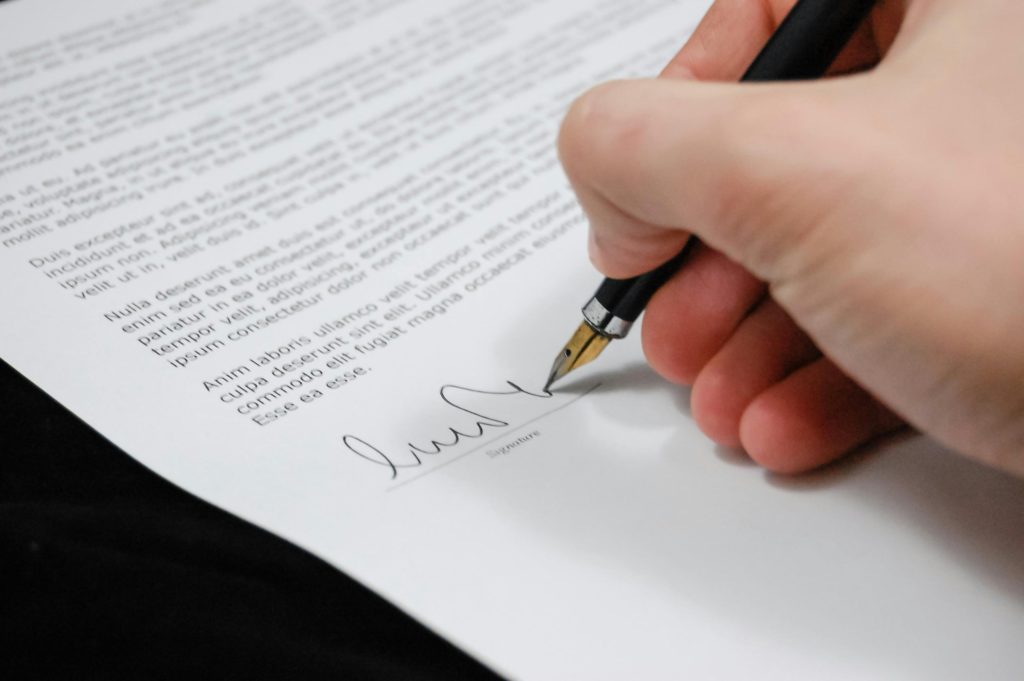 Beginner's guide to checking freelance contracts. Photo of a hand singing a contract.