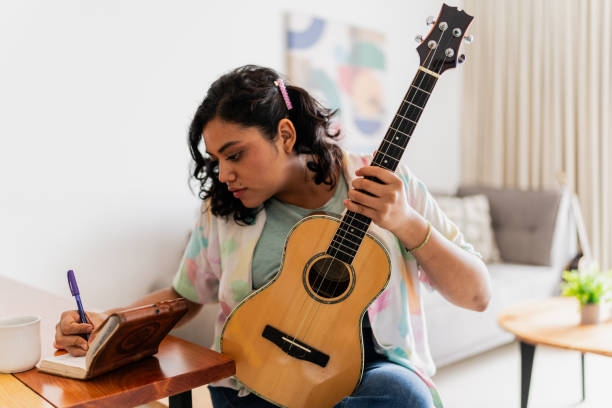 Behind the music - exploring the songwriting process of successful artists. Photo of a girl writing lyrics while holding a guitar.