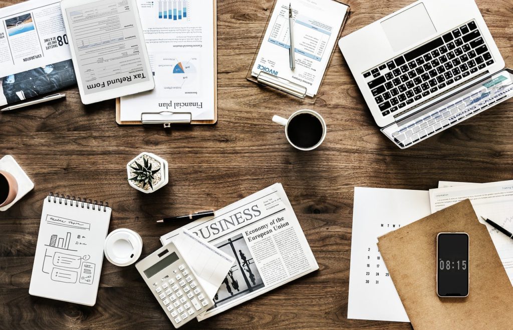 Why it's important to check if a business name is already in use before taking it. Photo of a laptop, smartphone, newspaper and files on a desk.