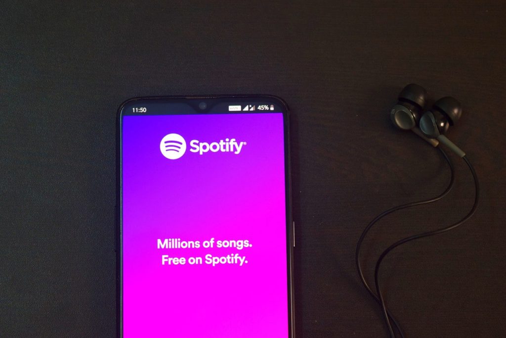 How to get a cheaper Spotify music subscription. A photo of a smartphone next to some earphones. The smartphone has a Spotify page loaded, saying "Millions of songs. Free on Spotify."