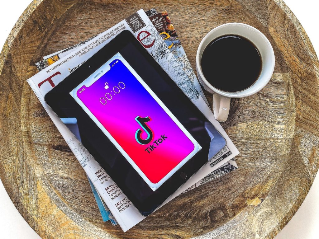 TikTok's 'browse as guest' option. Wooden table with books piled and a tablet with TikTok's logo loaded. Next to it is a cup of coffee.