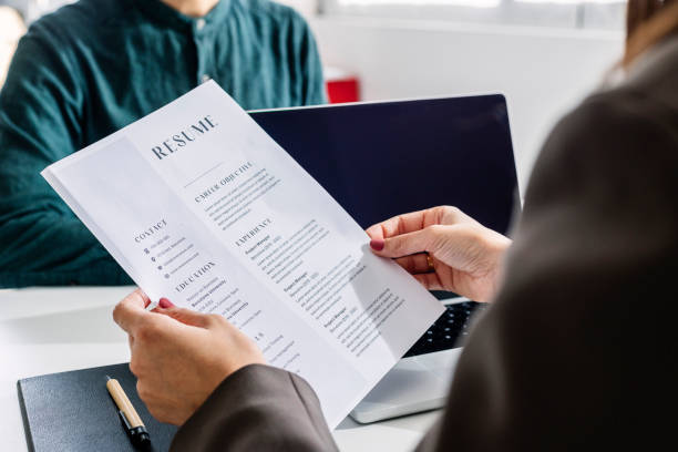 How to write an effective resume. Photo of someone holding a resume up, sat opposite someone with a laptop.