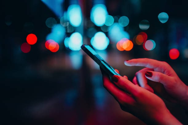 Essential tools for content creators - from editing software to analytics. Out of focus background lights. In the foreground is a hand holding a phone.