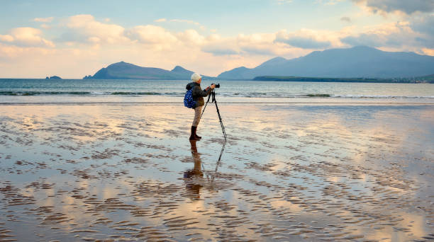 Simple photo projects to build your portfolio. Photo of someone with a tripod and camera photographing the sea on the beach.