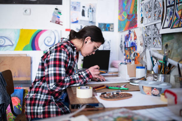 Essential equipment for art University - what you need to get started. Photo of a female student at her desk drawing. Lots of drawings surrounding her on the walls.