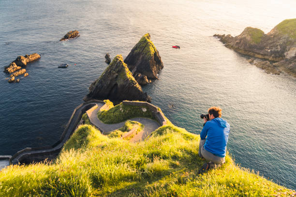 How technology is changing the photography industry - what small businesses need to know. Photo of a person crouched down on a cliff edge taking a photograph of the sea.