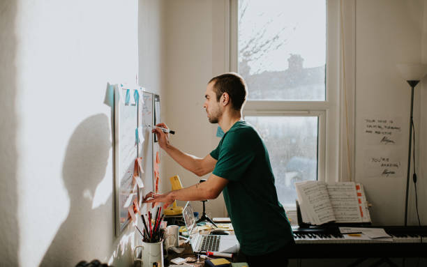 Content planning advice - how to stay organised and consistent as a creator. Photo of a guy writing on a whiteboard with sticky notes covering it, above a messy desk.