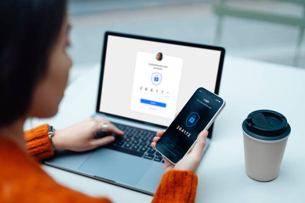 Protect your whole family with a free trial of 1Password for families. Photo of someone holding a phone with numbers on, sat in front of a laptop typing in a OTP.