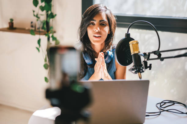 How to improve your on-camera presence for videos - tips to shine in front of the lens. Photo of a woman talking to a smartphone camera set up on a tripod with a microphone and laptop in front of her.