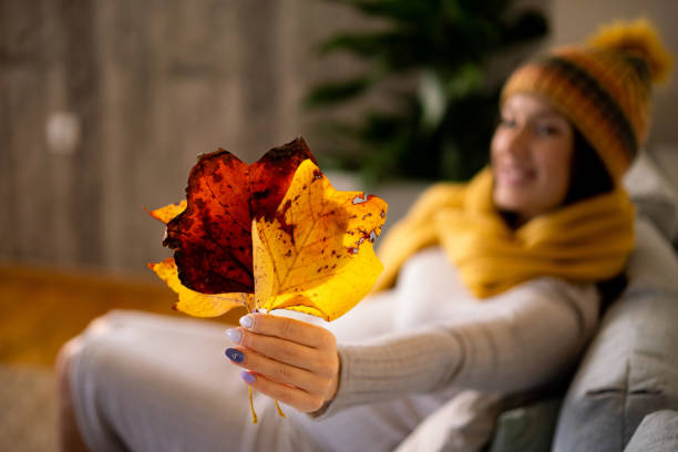 4. Behind-the-scenes content with a Fall twist. Woman holding leaves up to a camera while sat on the sofa.