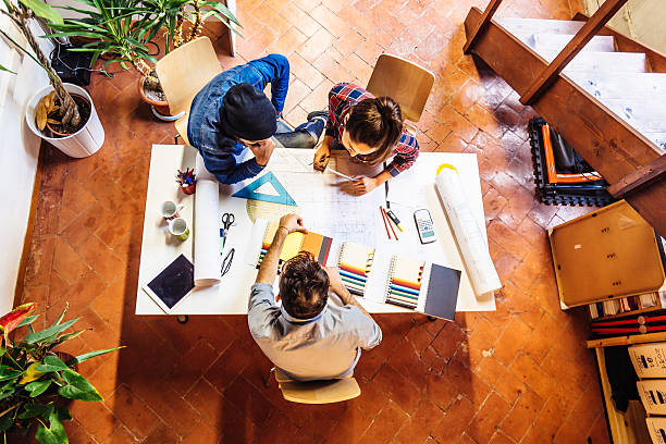 How to find clients as a creative brand. Photo from above of three people sat at a table discussing plans with art supplies.