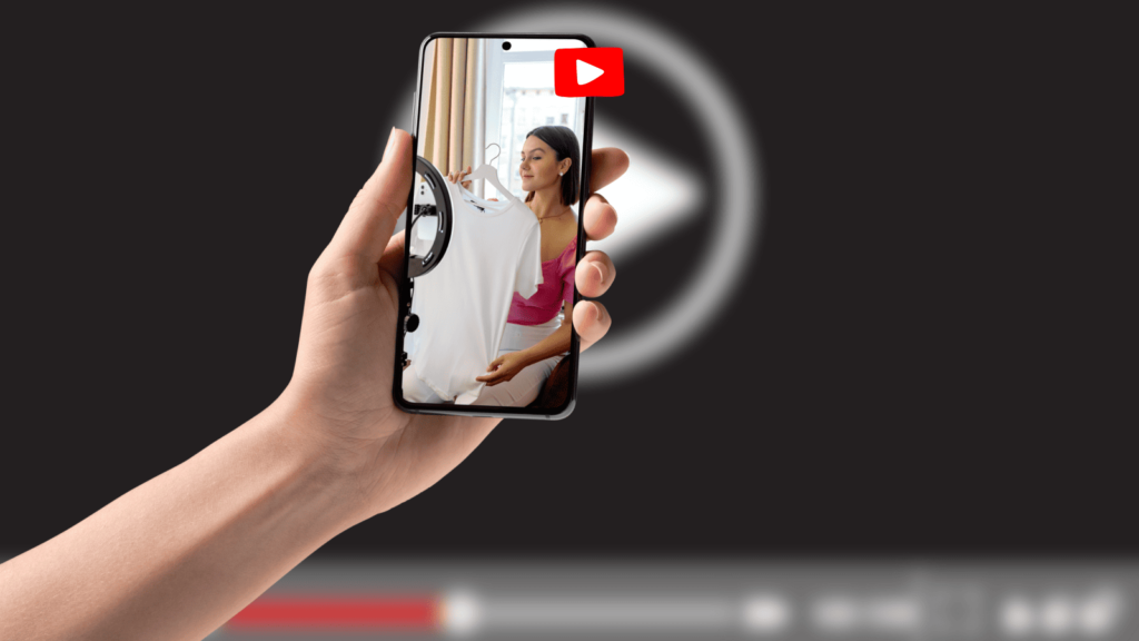 YouTube Shorts are expanding to 1-minute limits. Blurry background of a YouTube video. In the foreground is a hand holding a smartphone with a vlog loaded.